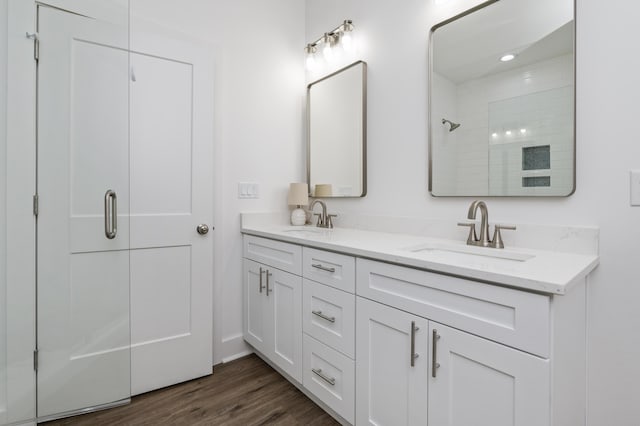 bathroom featuring double vanity, tiled shower, a sink, and wood finished floors