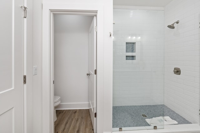 full bath with a tile shower, wood finished floors, toilet, and baseboards