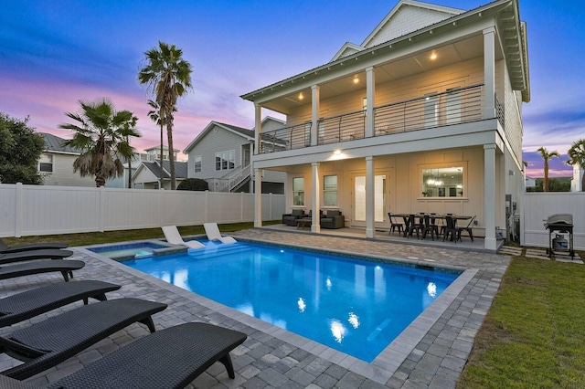 back of property at dusk with board and batten siding, a patio area, a balcony, a fenced backyard, and an outdoor living space