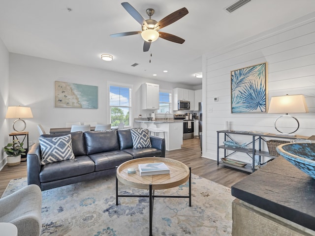 living area with ceiling fan, recessed lighting, wooden walls, wood finished floors, and visible vents