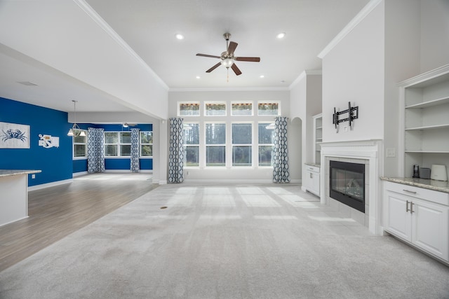 unfurnished living room with a tiled fireplace, built in features, ceiling fan, and crown molding