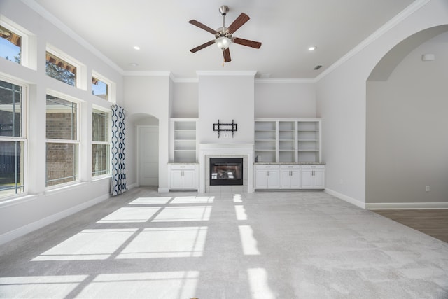 unfurnished living room with built in shelves, ceiling fan, ornamental molding, and light carpet