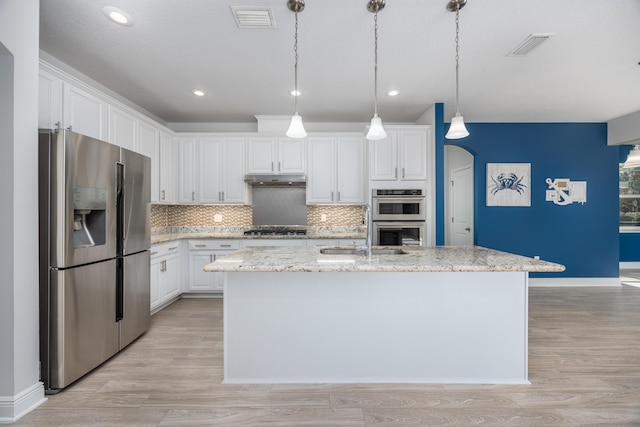 kitchen with decorative light fixtures, white cabinets, light stone counters, a center island with sink, and appliances with stainless steel finishes