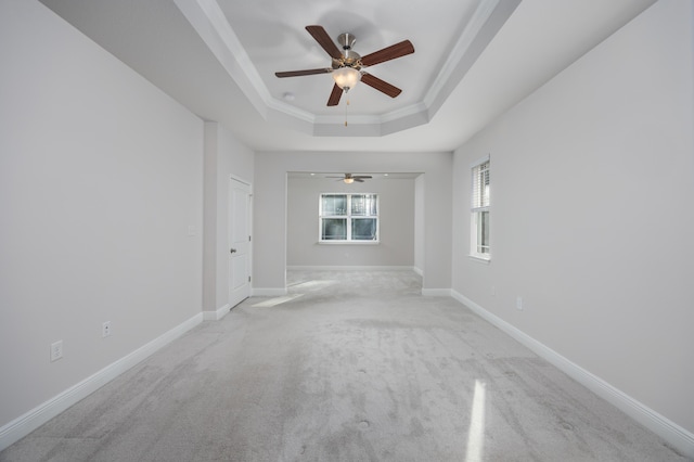 unfurnished room featuring a raised ceiling, ceiling fan, ornamental molding, and light colored carpet