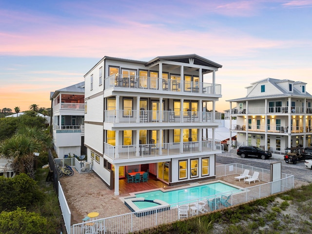 back house at dusk with a swimming pool with hot tub, a balcony, and a patio area