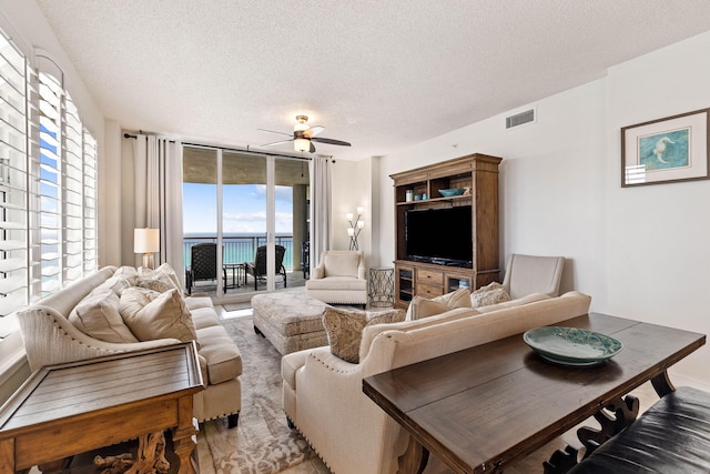 living room with ceiling fan, a textured ceiling, and a wall of windows