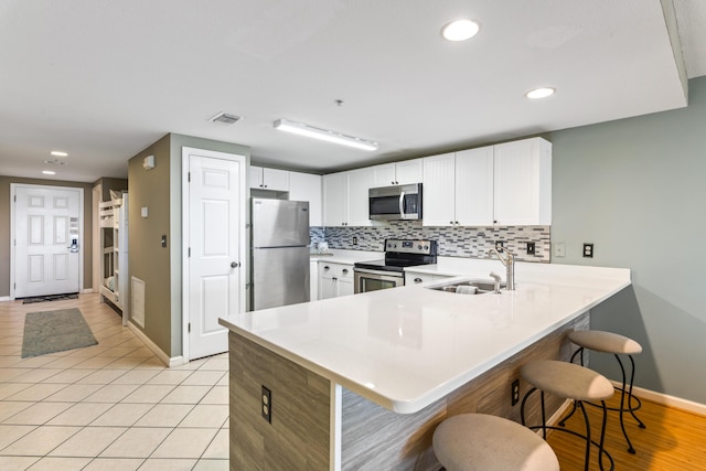 kitchen with stainless steel appliances, a peninsula, light countertops, and white cabinetry