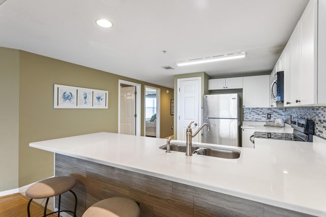 kitchen with stainless steel appliances, light countertops, white cabinets, a sink, and a peninsula