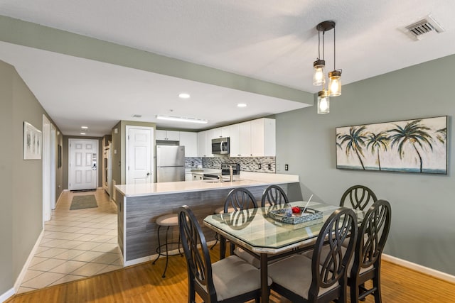 dining space featuring light wood-style floors, baseboards, visible vents, and recessed lighting