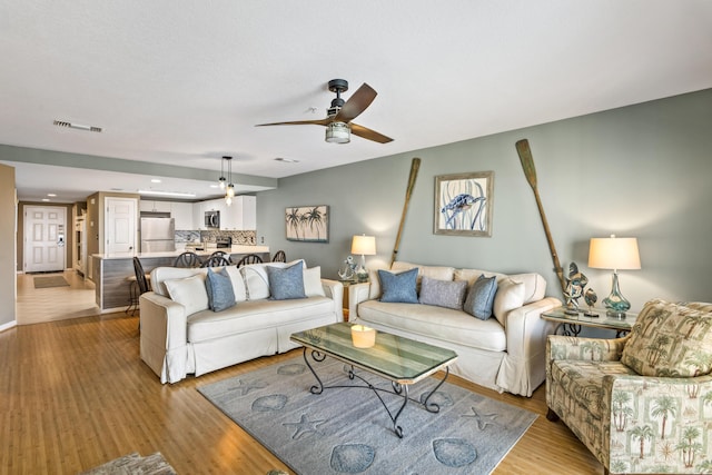 living room with a ceiling fan, visible vents, and light wood-style flooring