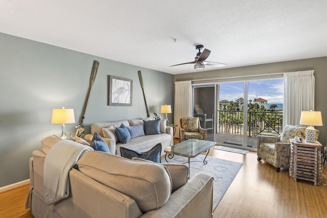 living room with baseboards, ceiling fan, a textured ceiling, and light wood finished floors