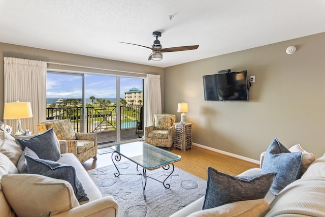 living room with a textured ceiling, light wood finished floors, a ceiling fan, and baseboards