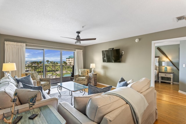 living area with a textured ceiling, ceiling fan, wood finished floors, visible vents, and baseboards