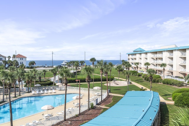 pool featuring a patio, a lawn, a water view, and fence