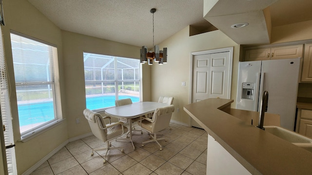 dining space featuring a notable chandelier, light tile patterned floors, a textured ceiling, vaulted ceiling, and sink