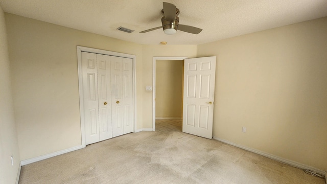 unfurnished bedroom featuring a closet, a textured ceiling, light colored carpet, and ceiling fan