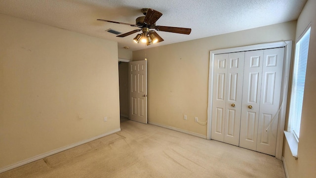 unfurnished bedroom featuring ceiling fan, a closet, light carpet, and a textured ceiling