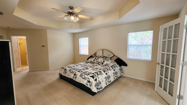 bedroom featuring ceiling fan, a raised ceiling, and light carpet