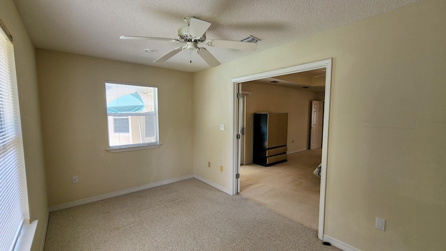 spare room featuring light carpet, ceiling fan, and a textured ceiling