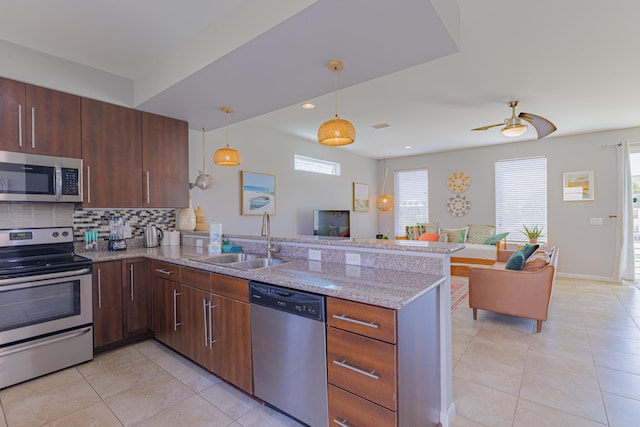 kitchen with appliances with stainless steel finishes, sink, kitchen peninsula, and light stone countertops