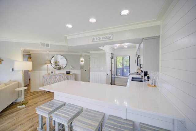 kitchen with crown molding, light wood-type flooring, stainless steel appliances, and kitchen peninsula