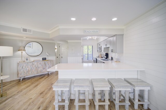 kitchen featuring a breakfast bar area, crown molding, stainless steel appliances, light hardwood / wood-style floors, and kitchen peninsula