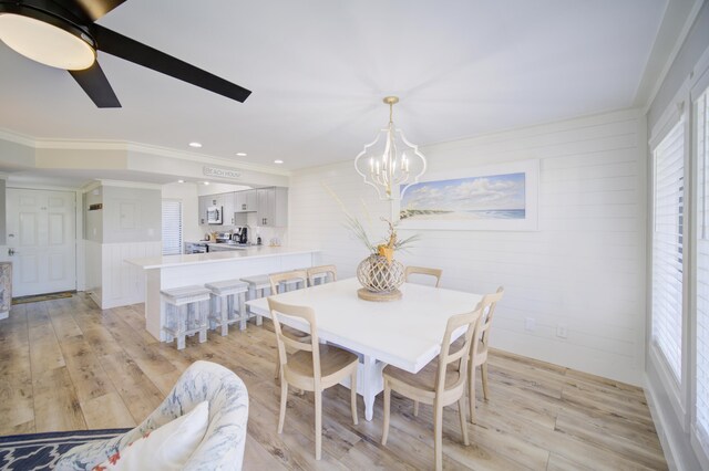 dining area featuring light wood-type flooring, a wealth of natural light, ceiling fan with notable chandelier, and crown molding