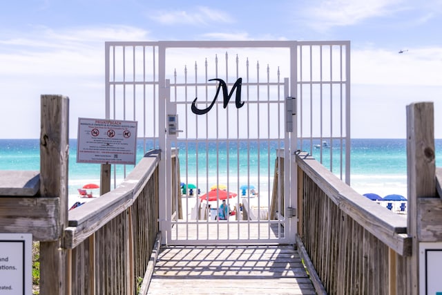 exterior space featuring a beach view, a water view, fence, and a gate