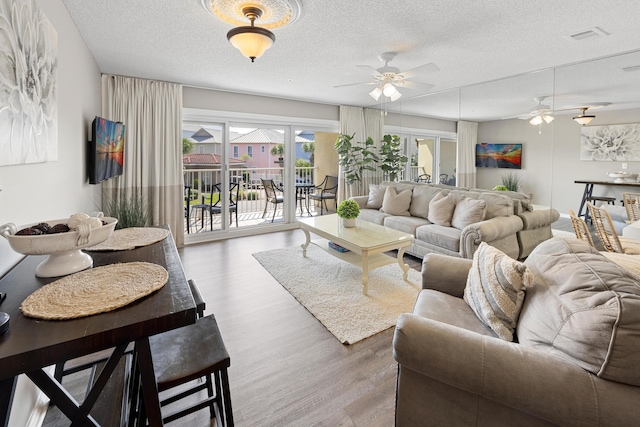 living area featuring visible vents, a textured ceiling, a ceiling fan, and wood finished floors