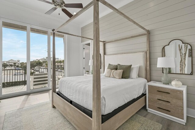 bedroom featuring expansive windows, dark wood-type flooring, access to exterior, and wood walls