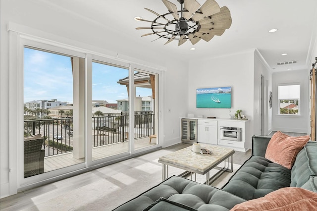 living room with crown molding, plenty of natural light, beverage cooler, and ceiling fan