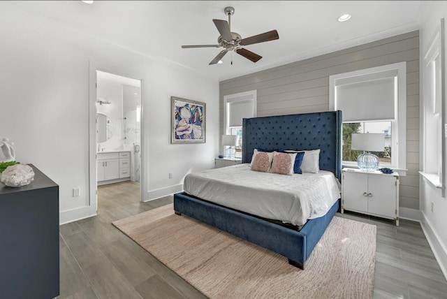 bedroom with connected bathroom, wood-type flooring, ceiling fan, and wood walls