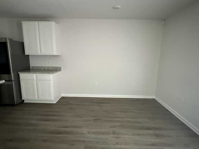 unfurnished dining area featuring dark wood-style flooring and baseboards