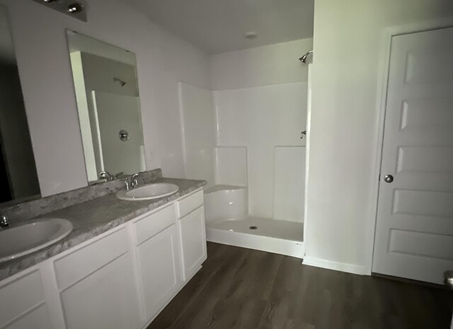 full bathroom featuring double vanity, wood finished floors, a stall shower, and a sink