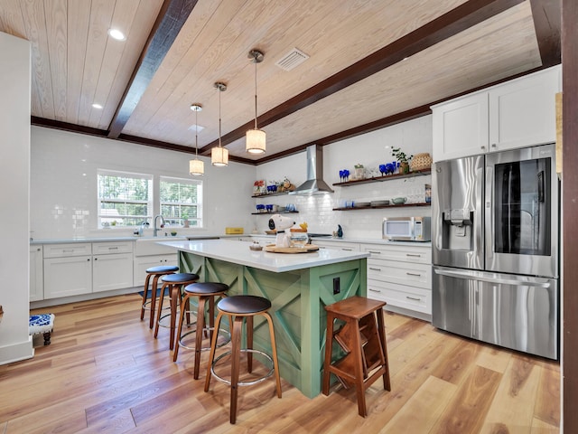 kitchen with beamed ceiling, wall chimney exhaust hood, light hardwood / wood-style floors, and appliances with stainless steel finishes