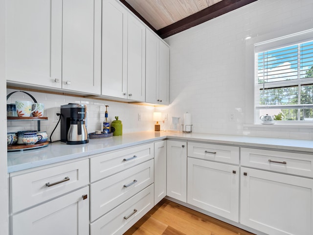 kitchen with beam ceiling, white cabinetry, light wood-type flooring, and decorative backsplash