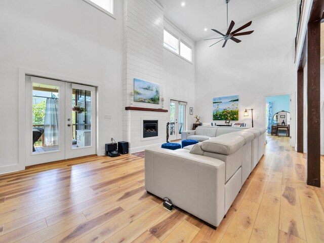 living room with a large fireplace, ceiling fan, french doors, light hardwood / wood-style flooring, and a towering ceiling