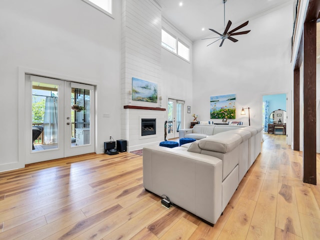 living room with ceiling fan, a large fireplace, light wood-type flooring, and french doors