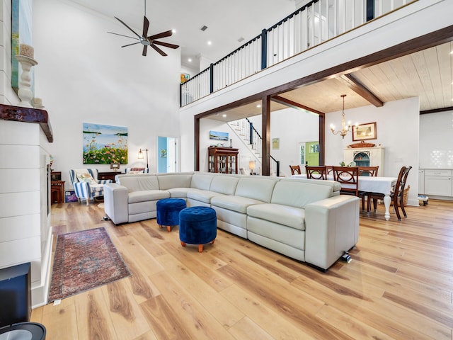 living room with beam ceiling, ceiling fan with notable chandelier, a towering ceiling, and light wood-type flooring