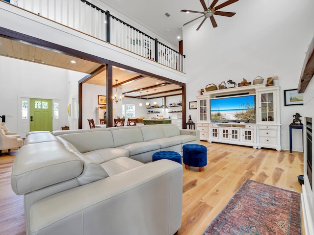 living room featuring ceiling fan with notable chandelier, a towering ceiling, and light hardwood / wood-style flooring