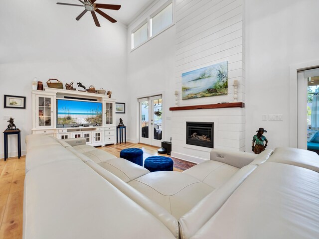 living room with a fireplace, ceiling fan, french doors, light hardwood / wood-style flooring, and a towering ceiling