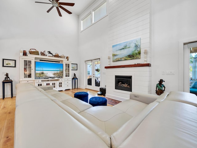 living room featuring hardwood / wood-style flooring, ceiling fan, a high ceiling, a large fireplace, and french doors