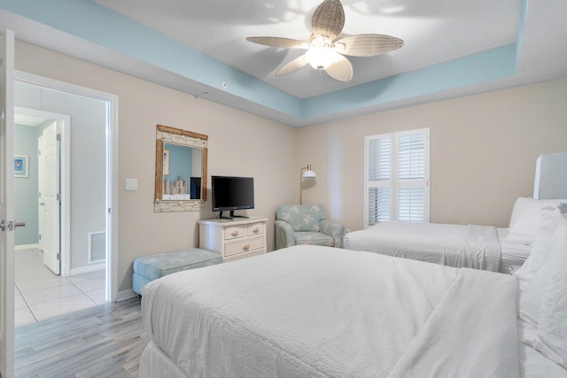 bedroom with a raised ceiling, light hardwood / wood-style flooring, ensuite bathroom, and ceiling fan