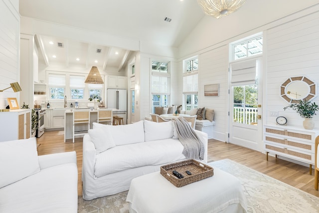 living room featuring high vaulted ceiling, sink, and light hardwood / wood-style floors