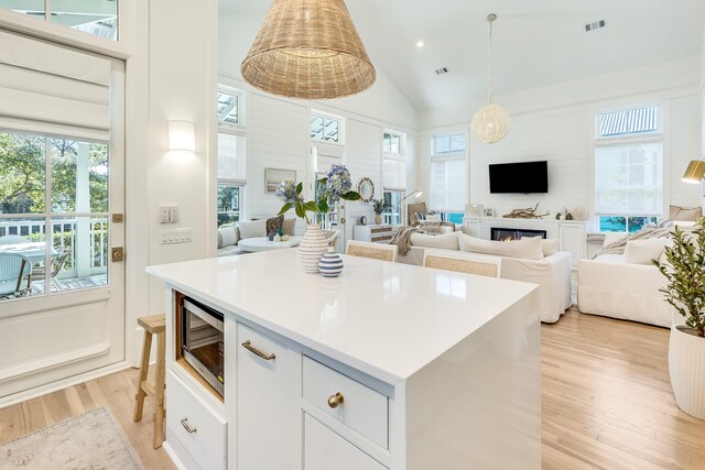 kitchen with stainless steel microwave, hanging light fixtures, white cabinets, a kitchen island, and light wood-type flooring