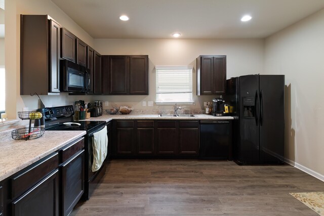 kitchen featuring sink, dark brown cabinets, dark hardwood / wood-style flooring, and black appliances