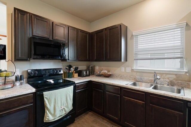 kitchen featuring sink, wood-type flooring, dark brown cabinets, and black appliances