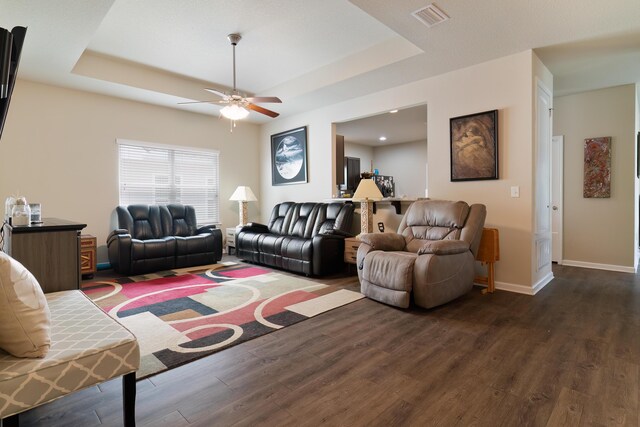 living room with ceiling fan, a raised ceiling, and dark hardwood / wood-style floors