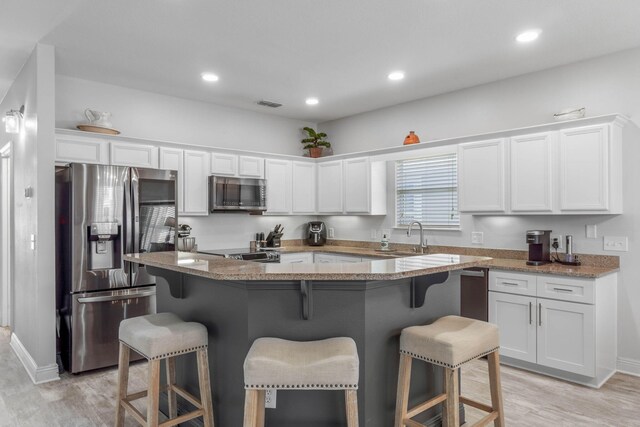 kitchen featuring a breakfast bar area, white cabinetry, stainless steel appliances, light hardwood / wood-style floors, and a kitchen island