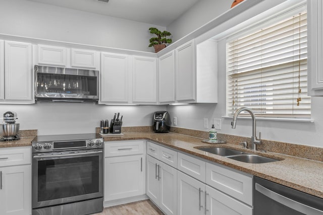 kitchen featuring light wood-type flooring, white cabinets, appliances with stainless steel finishes, stone countertops, and sink